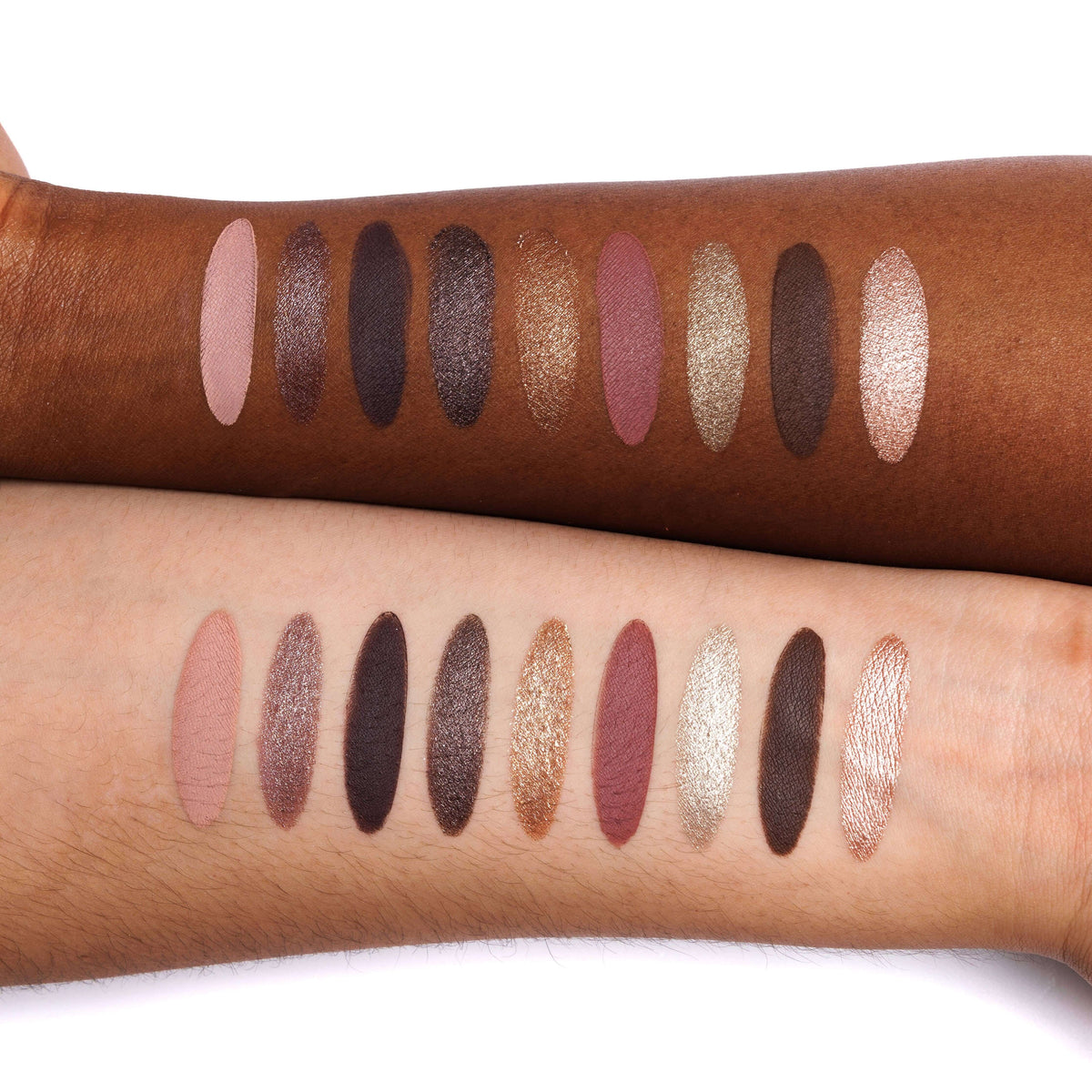 Two forearms displaying vertical rows of eyeshadow swatches in various matte, shimmer, and glitter finishes and shades, including dusty pink, charcoal, bronze, gold, taupe, and rose gold tones, set against a plain white background.