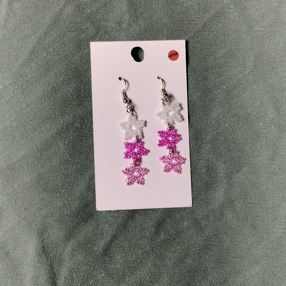 Pair of pink and white floral earrings on a card against a gray fabric background