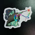 Sticker of a cartoon character in a witch hat with a colorful wand on a black background