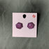 Purple polyhedral dice earrings on a pink card against a green background