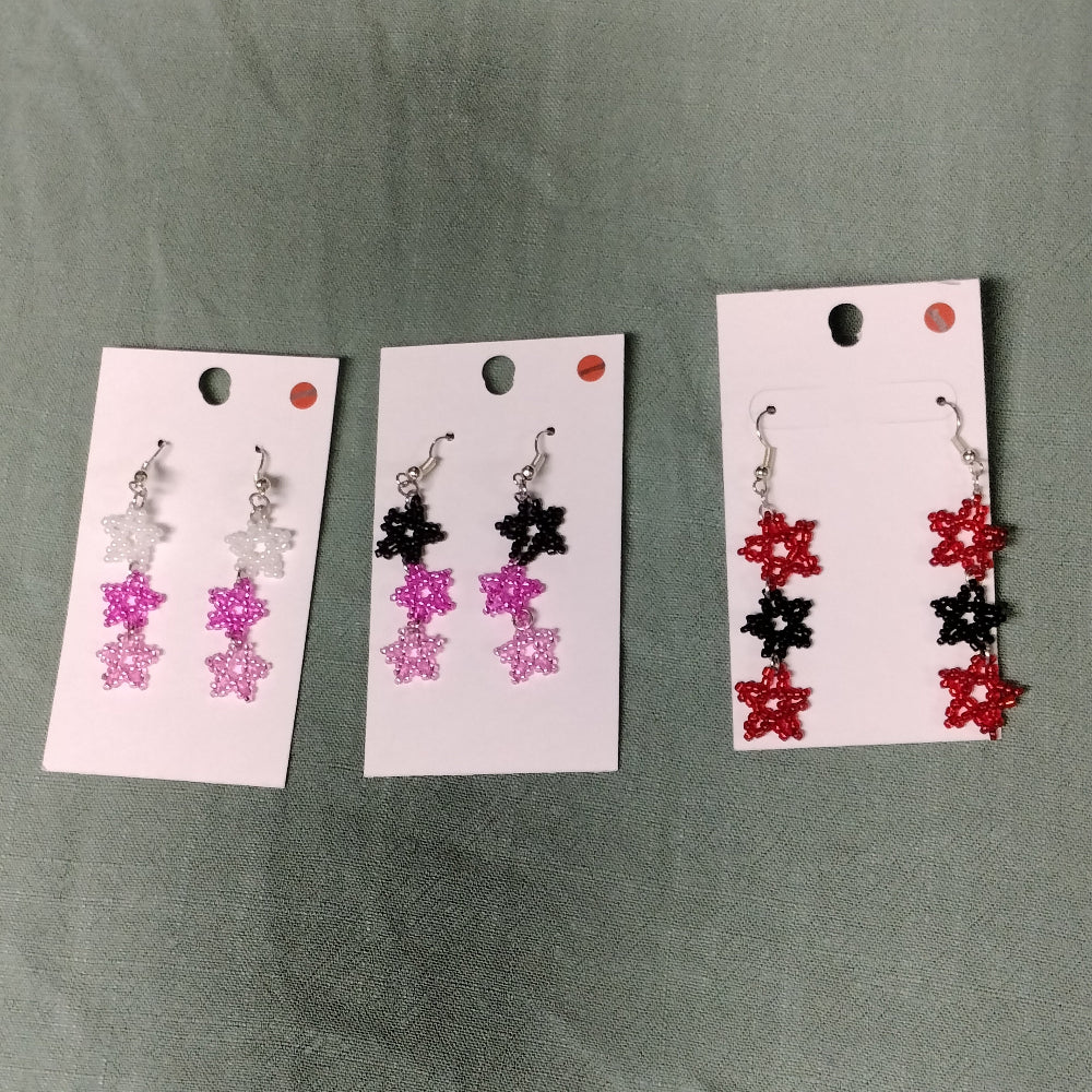 Three sets of beaded earrings on display cards against a green background