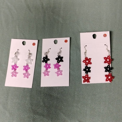 Three sets of beaded earrings on display cards against a green background
