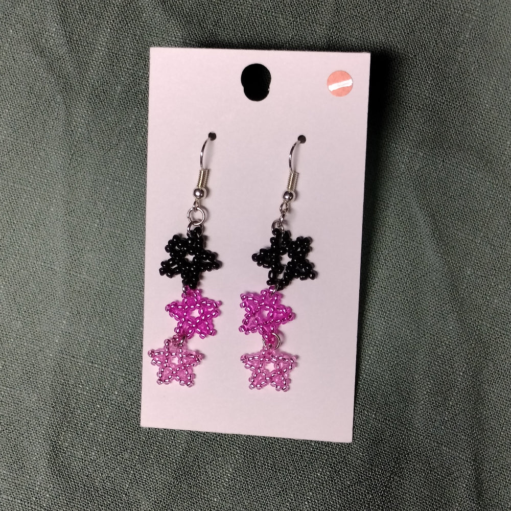 Pair of black and pink beaded earrings on a card against a gray background
