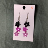 Pair of black and pink beaded earrings on a card against a gray background