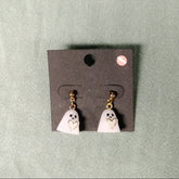 Ghost-shaped earrings on a gray card against a green background